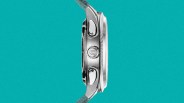 Side view of a silver stainless steel watch case with two push buttons and a crown on a teal woven strap.