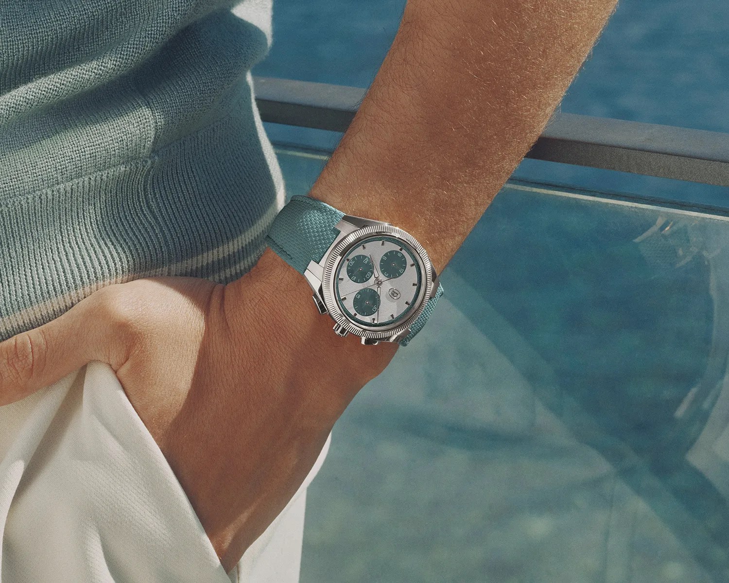 Silver chronograph wristwatch with teal subdials and textured teal strap worn on a wrist.