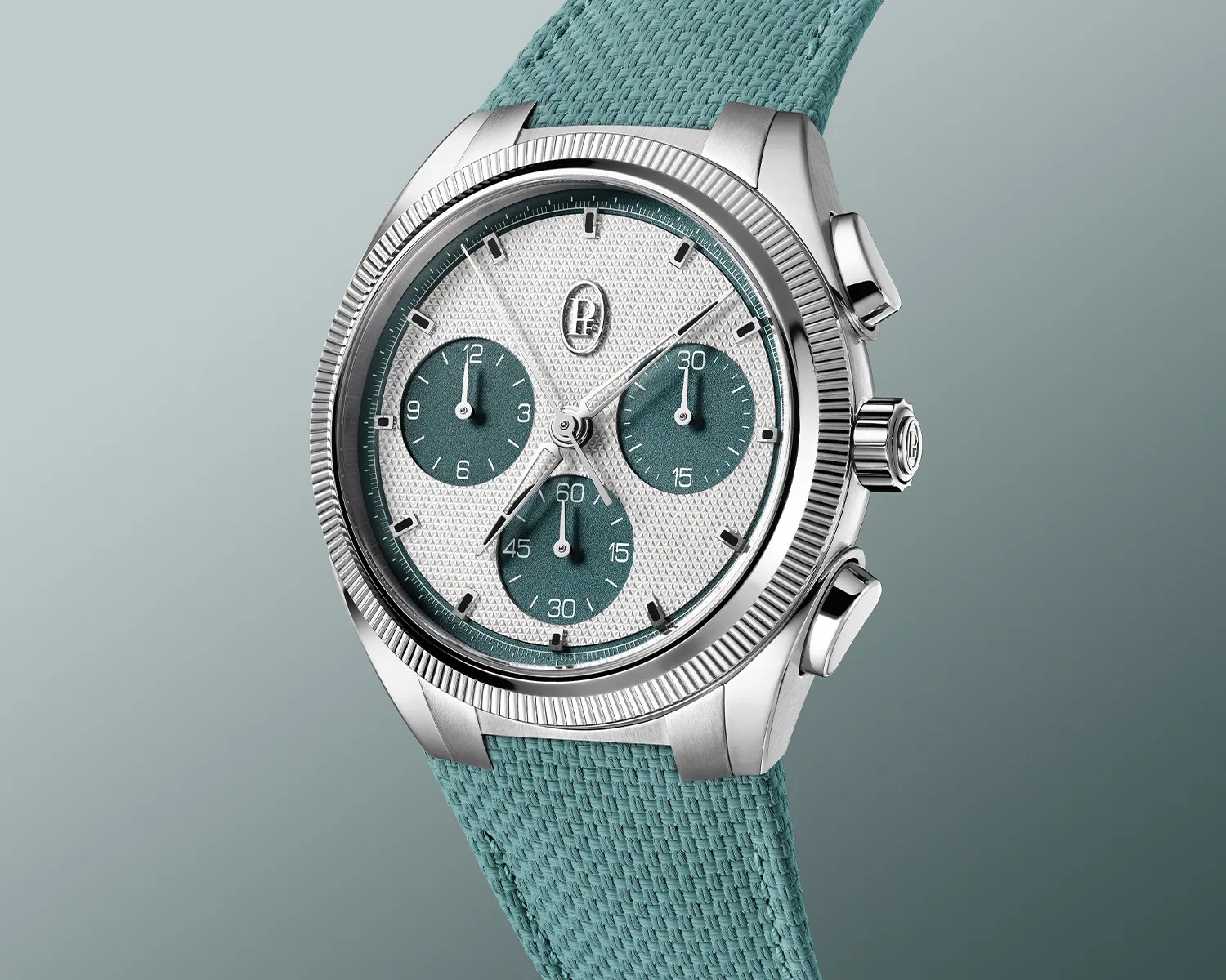 Silver chronograph wristwatch with textured white and teal dial and teal woven strap.