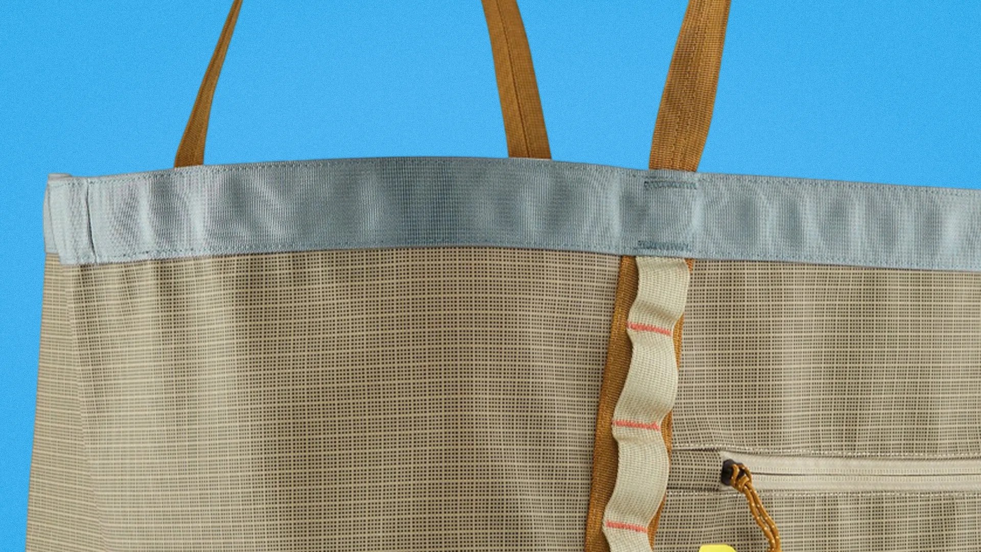 Beige mesh tote bag with light blue trim and brown handles against a blue background.