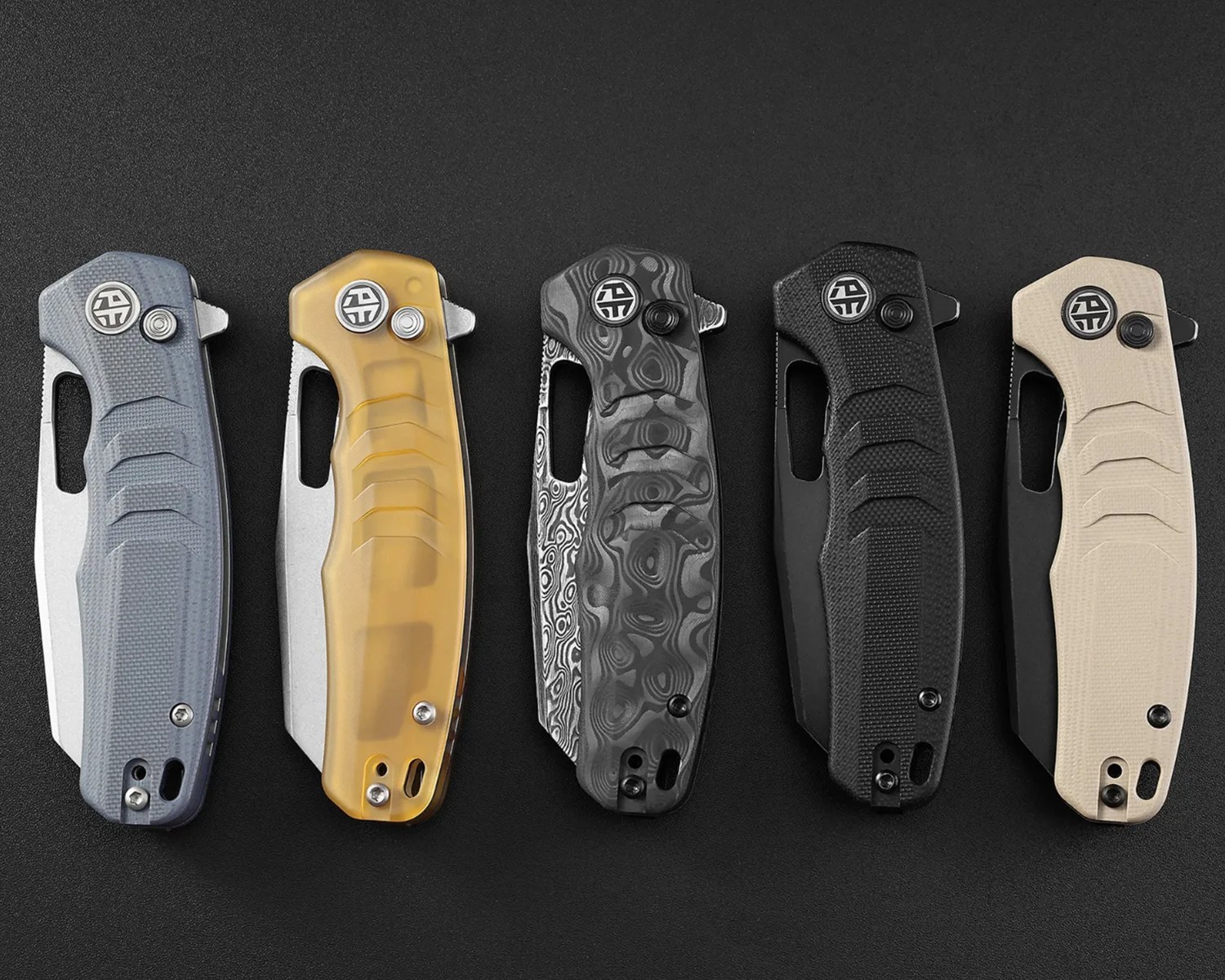 Five closed folding knives with textured handles in blue, translucent amber, black patterned, solid black, and beige, arranged side by side on a black surface.