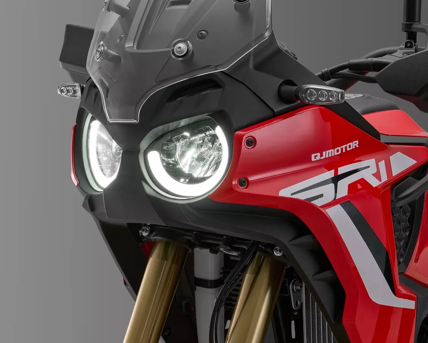 Close-up of a red QJMotor motorcycle front with dual round LED headlights and gold front forks.