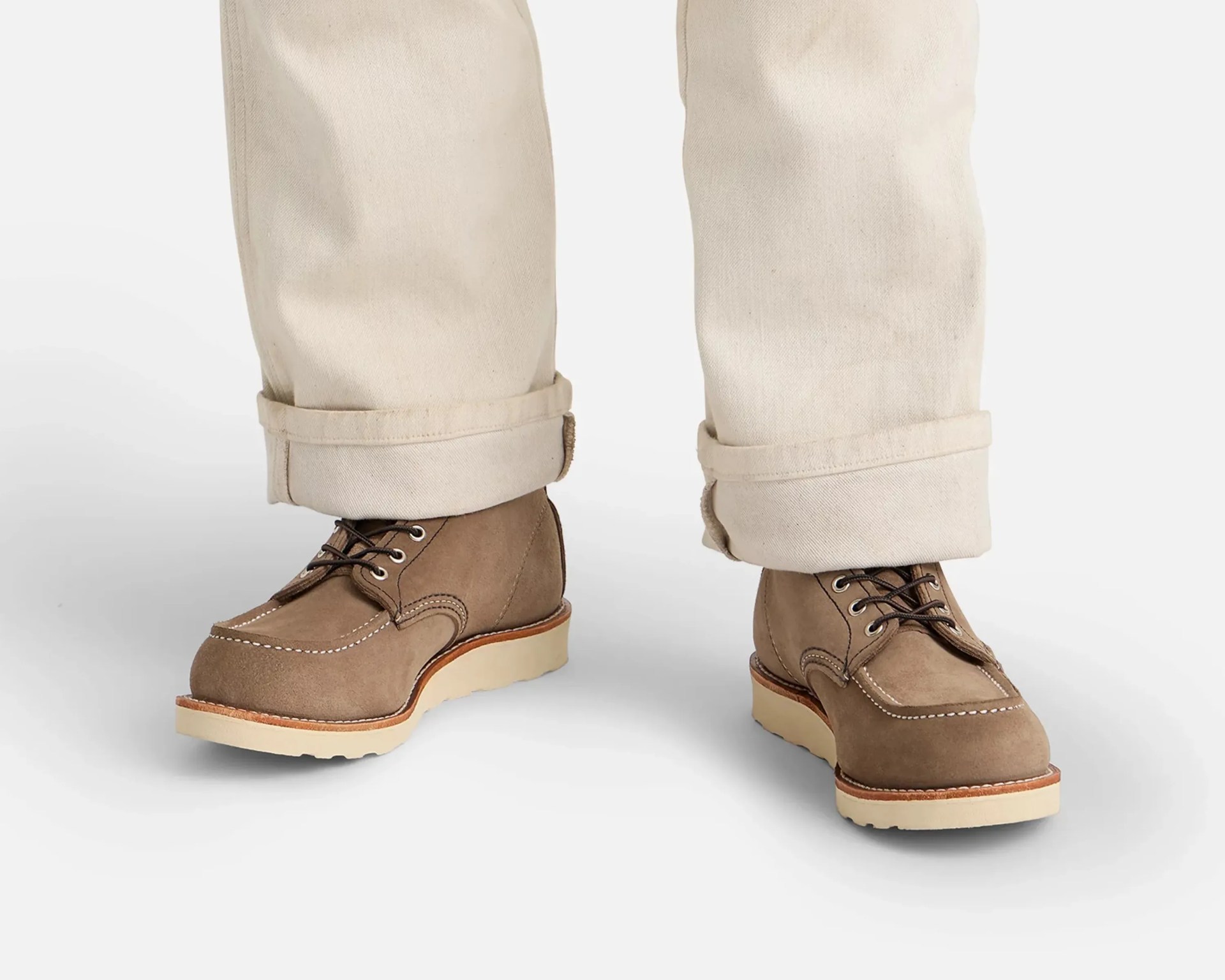 Pair of brown suede moc toe boots with white stitching and cream wedge soles worn with rolled-up beige pants.