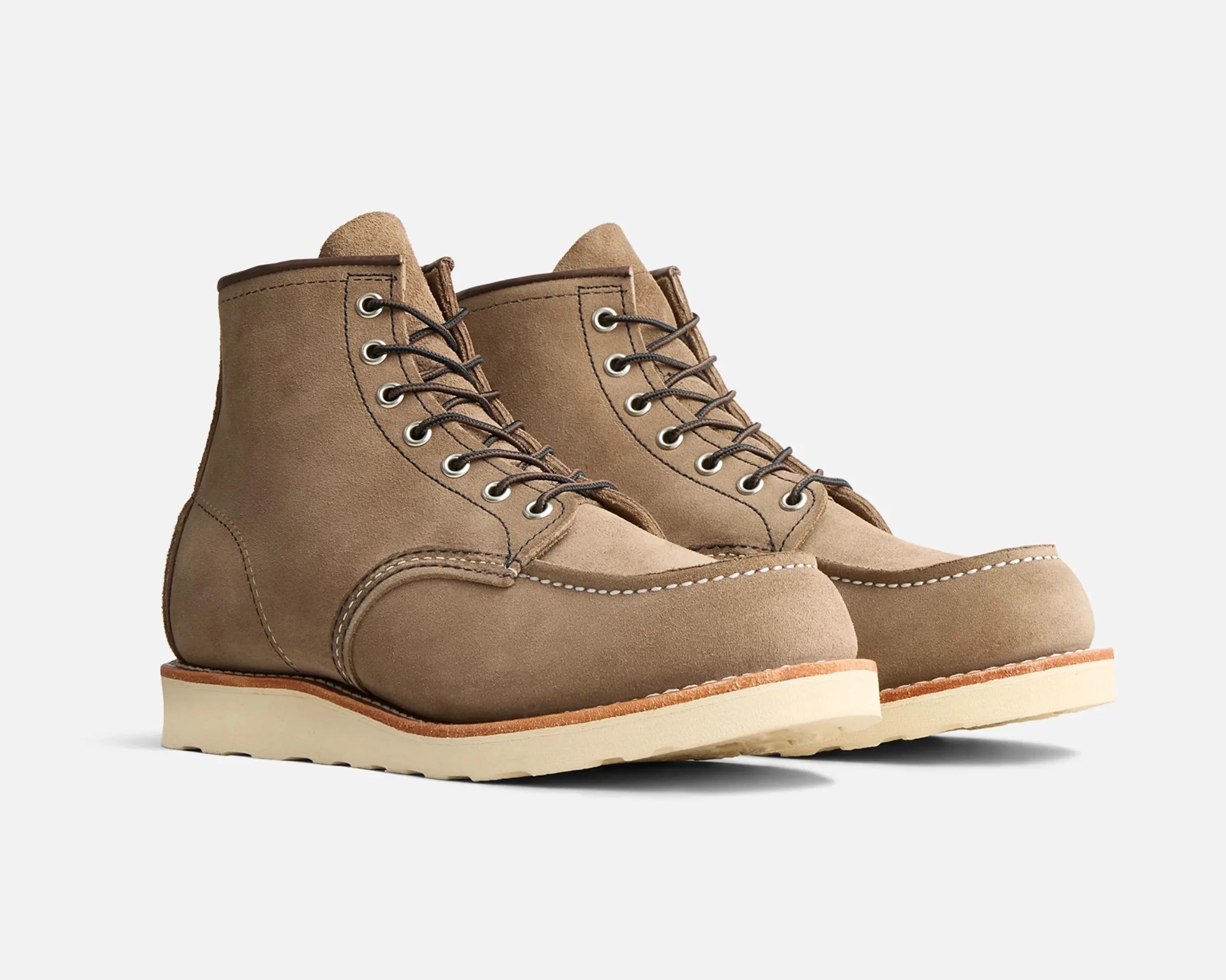 Pair of tan suede moc toe boots with white stitching and cream rubber soles on a white background.
