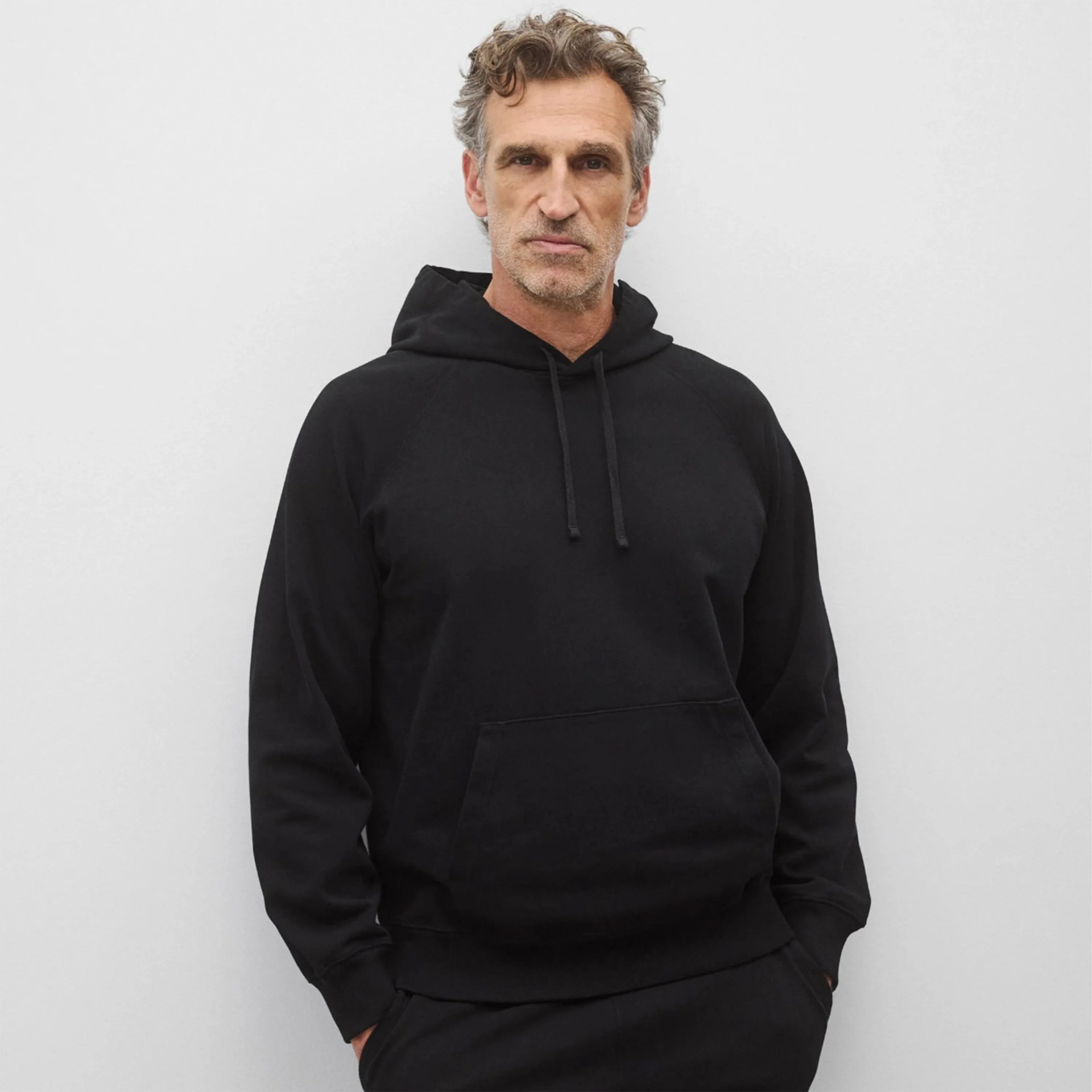 Black pullover hoodie with front kangaroo pocket worn by a person against a plain light gray background.