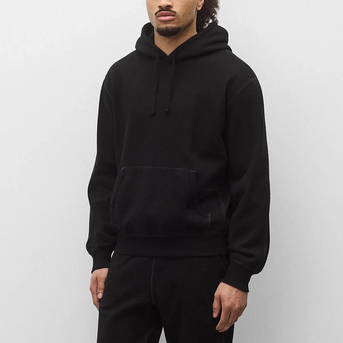 Black pullover hoodie with front kangaroo pocket worn by a person against a plain light background.