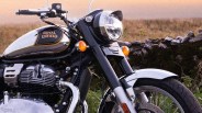 Close-up of a black and chrome Royal Enfield motorcycle front with headlight, orange indicators, and part of the fuel tank.