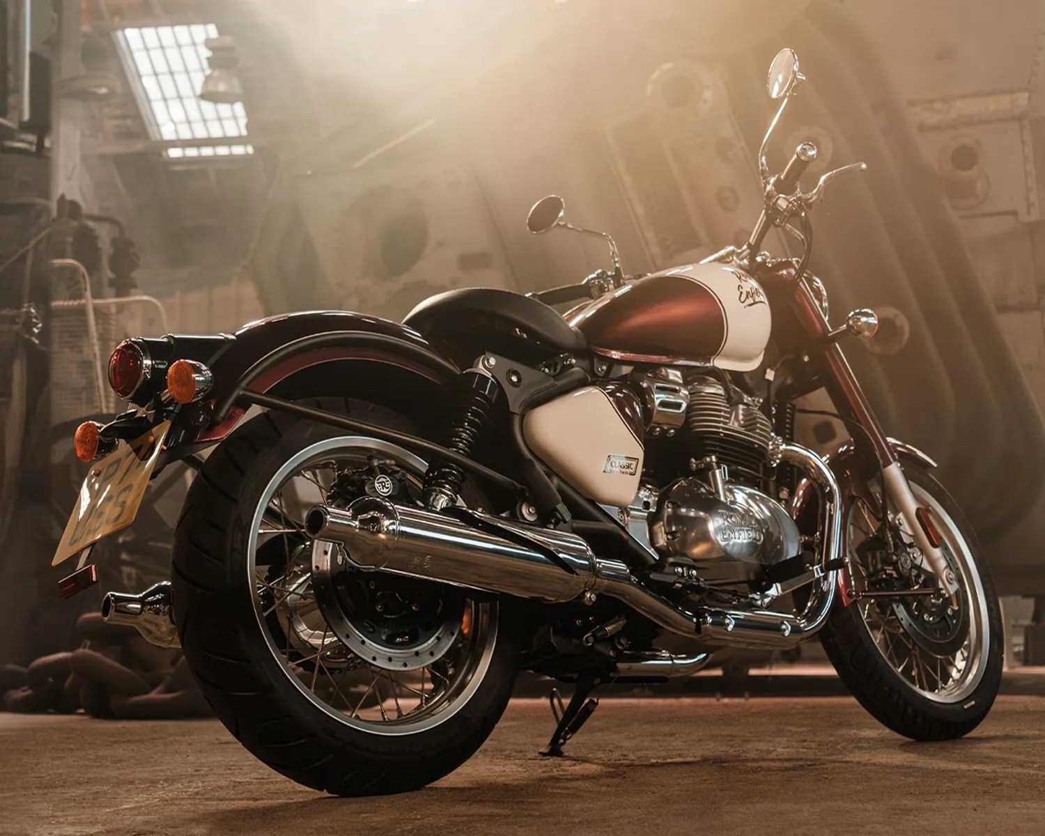 Maroon and white Royal Enfield Classic 350 motorcycle with chrome exhaust and black seat in an industrial setting.