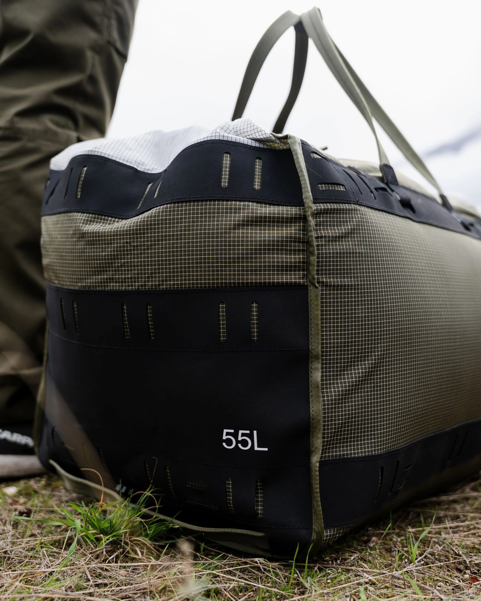 Olive green and black 55-liter duffel bag with grid pattern and handles on grass.