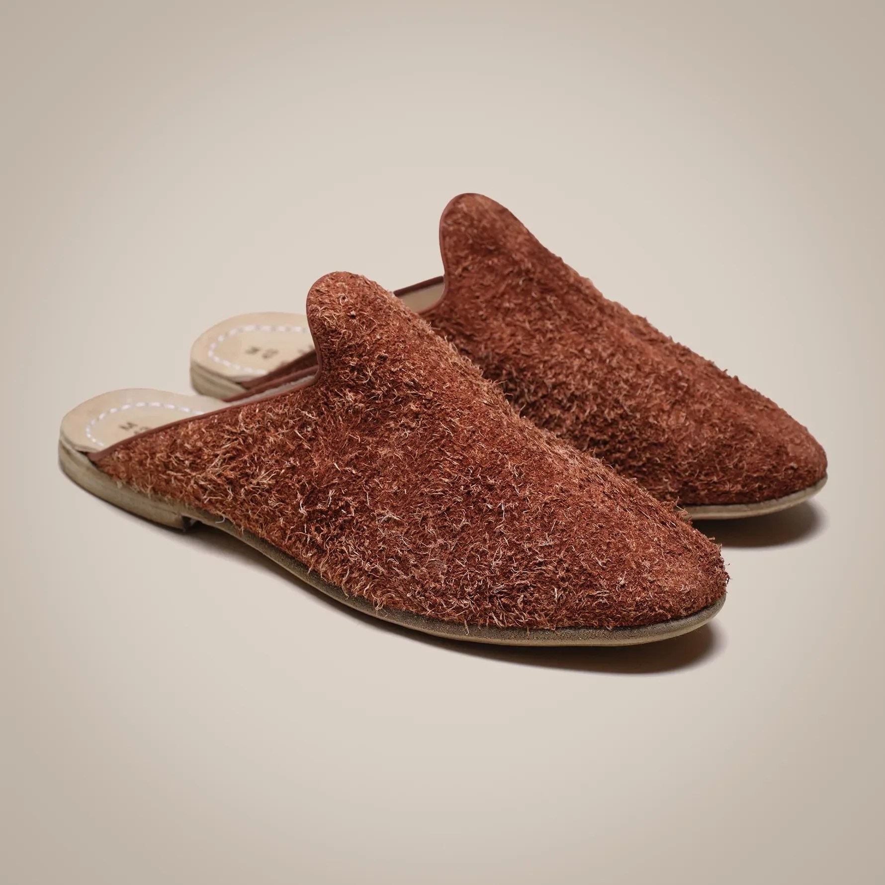 Pair of brown textured slip-on slippers with a rounded toe and flat sole on a beige background.