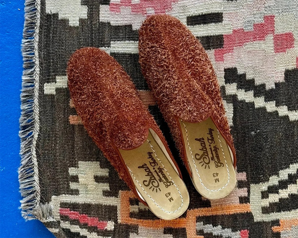 Pair of rust-colored textured slip-on shoes with "Sabah" branding on insoles, placed on a patterned rug.