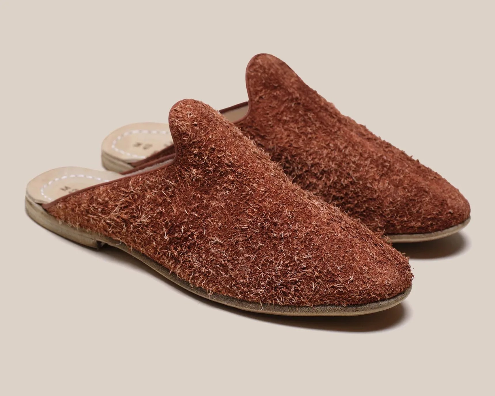 Pair of brown textured slip-on slippers with flat soles on a beige background.