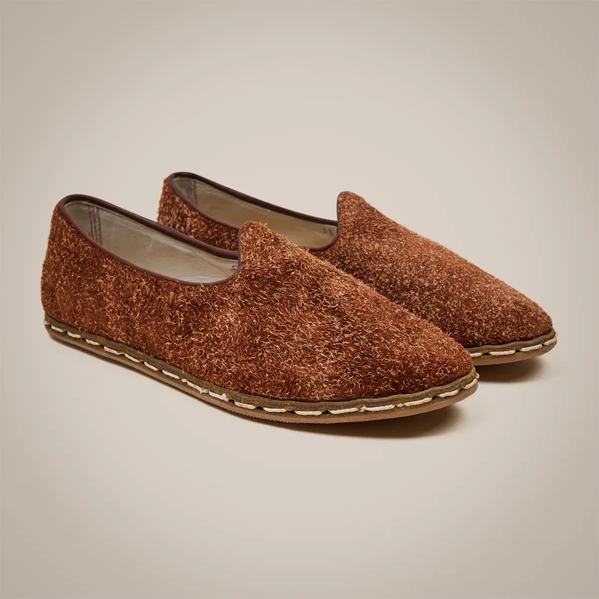 Pair of brown textured slip-on shoes with visible stitching along the sole on a neutral background.