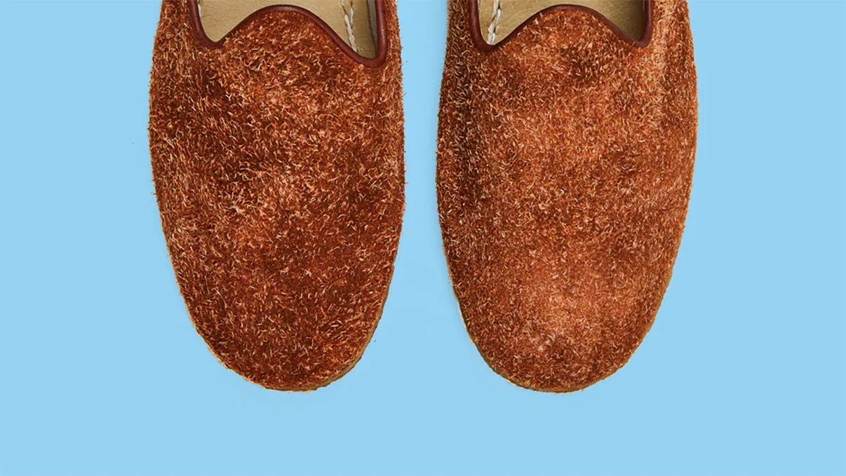 Pair of brown textured slip-on shoes with a fuzzy finish on a light blue background.