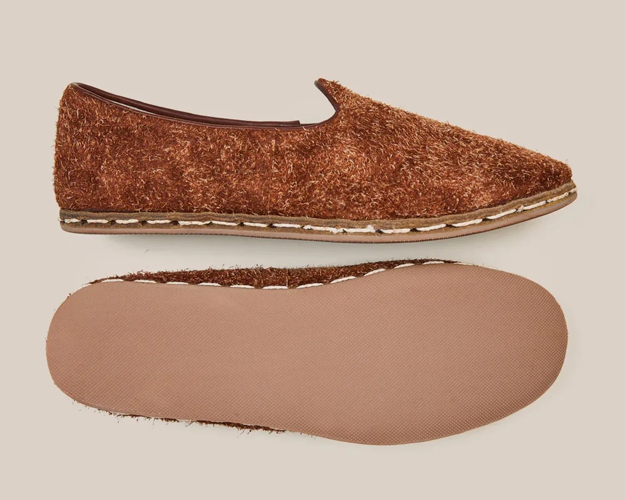 Pair of brown textured slip-on shoes with stitched midsoles and smooth rubber soles on a beige background.