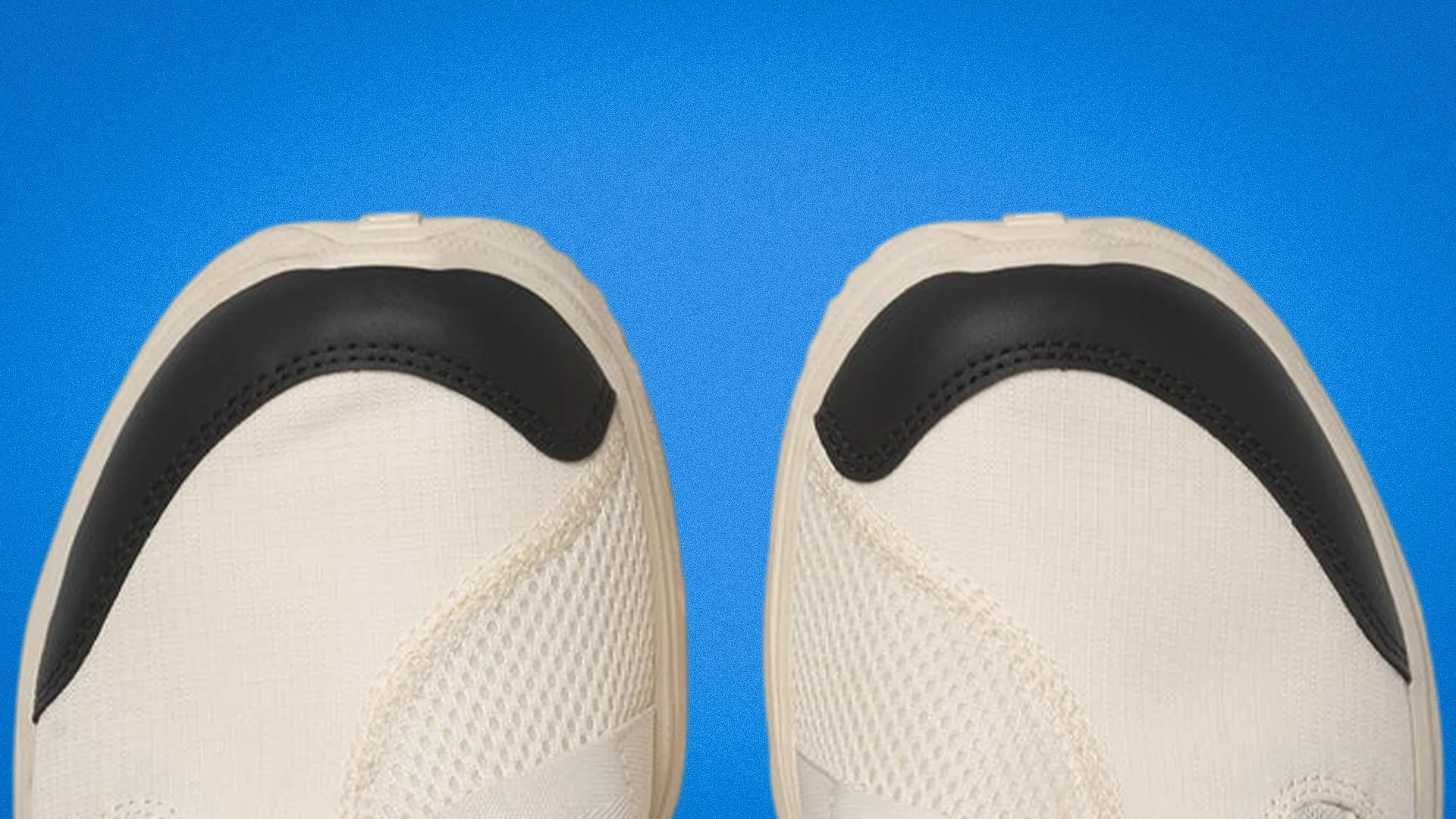 Close-up of beige sneakers with black toe caps against a blue background.