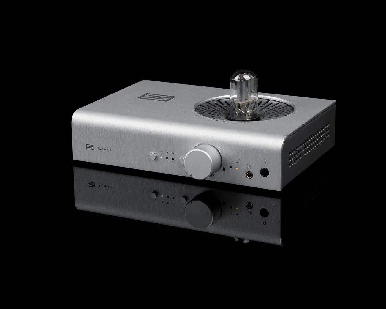 Silver metal audio amplifier with a large central knob and a visible vacuum tube on top, reflected on a black surface.