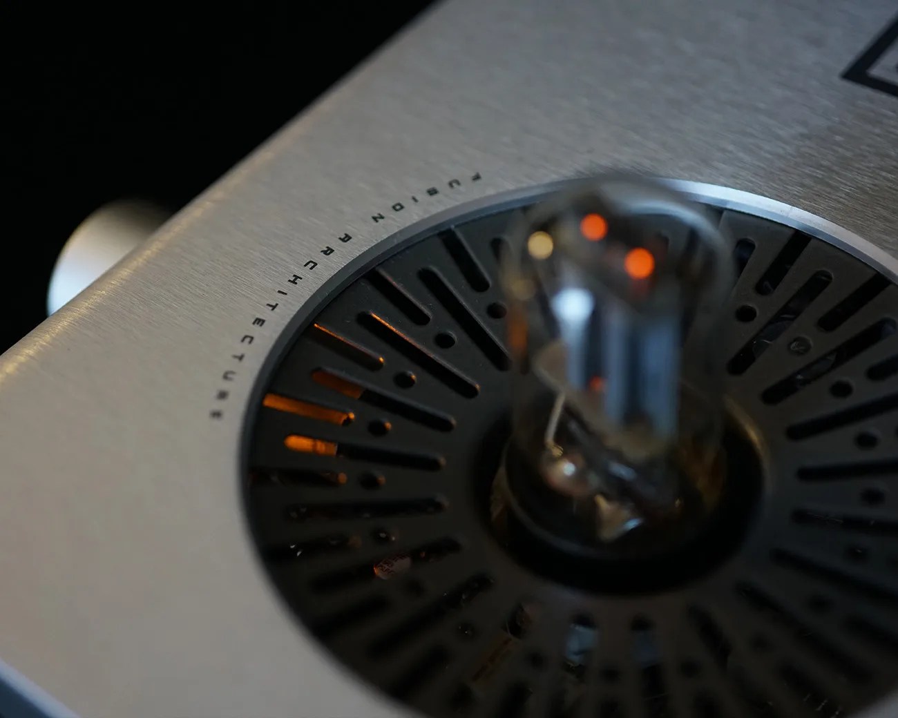 Close-up of a silver audio device with a glowing vacuum tube and black circular vent labeled "FUSION ARCHITECTURE.