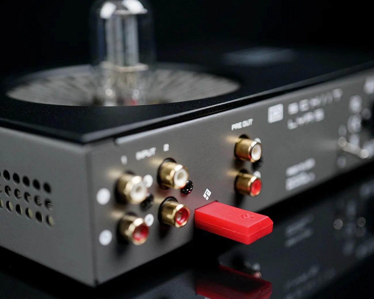 Close-up of a black audio device with gold RCA input/output ports and a red USB drive plugged in.