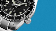 Close-up of a Seiko Marinemaster automatic diver's watch with a black dial and stainless steel bracelet on a blue background.