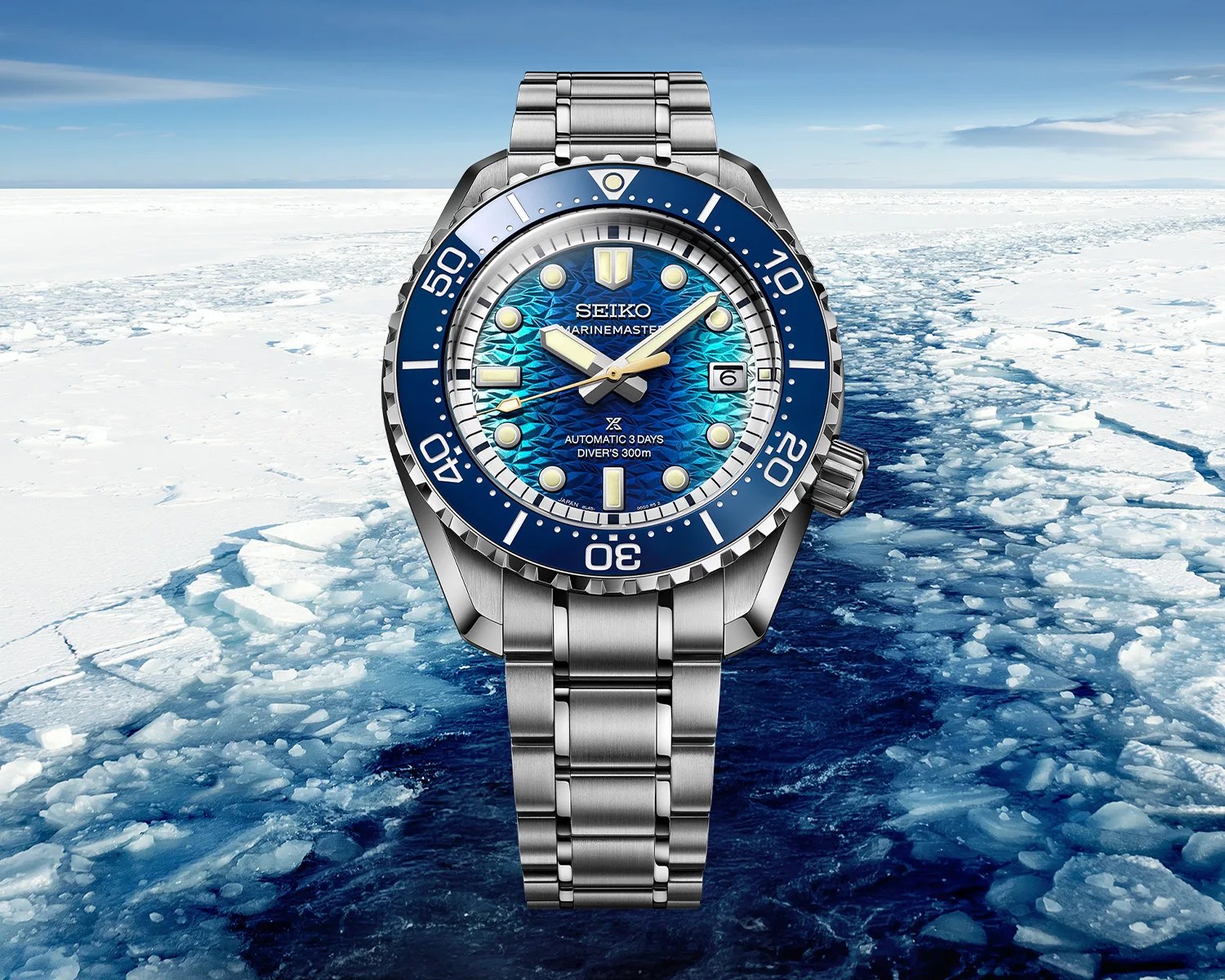 Silver Seiko Marinemaster dive watch with blue textured dial and rotating bezel over icy ocean background.