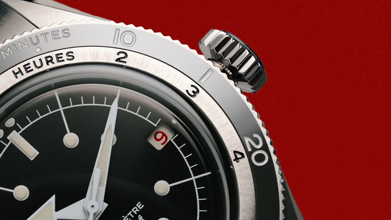 Close-up of a silver watch bezel and crown with a black dial showing white hands and a red number 9 date on a red background.