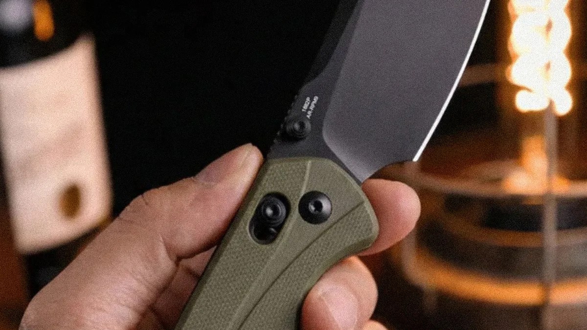 Hand holding a folding knife with an olive green textured handle and partially visible black blade.