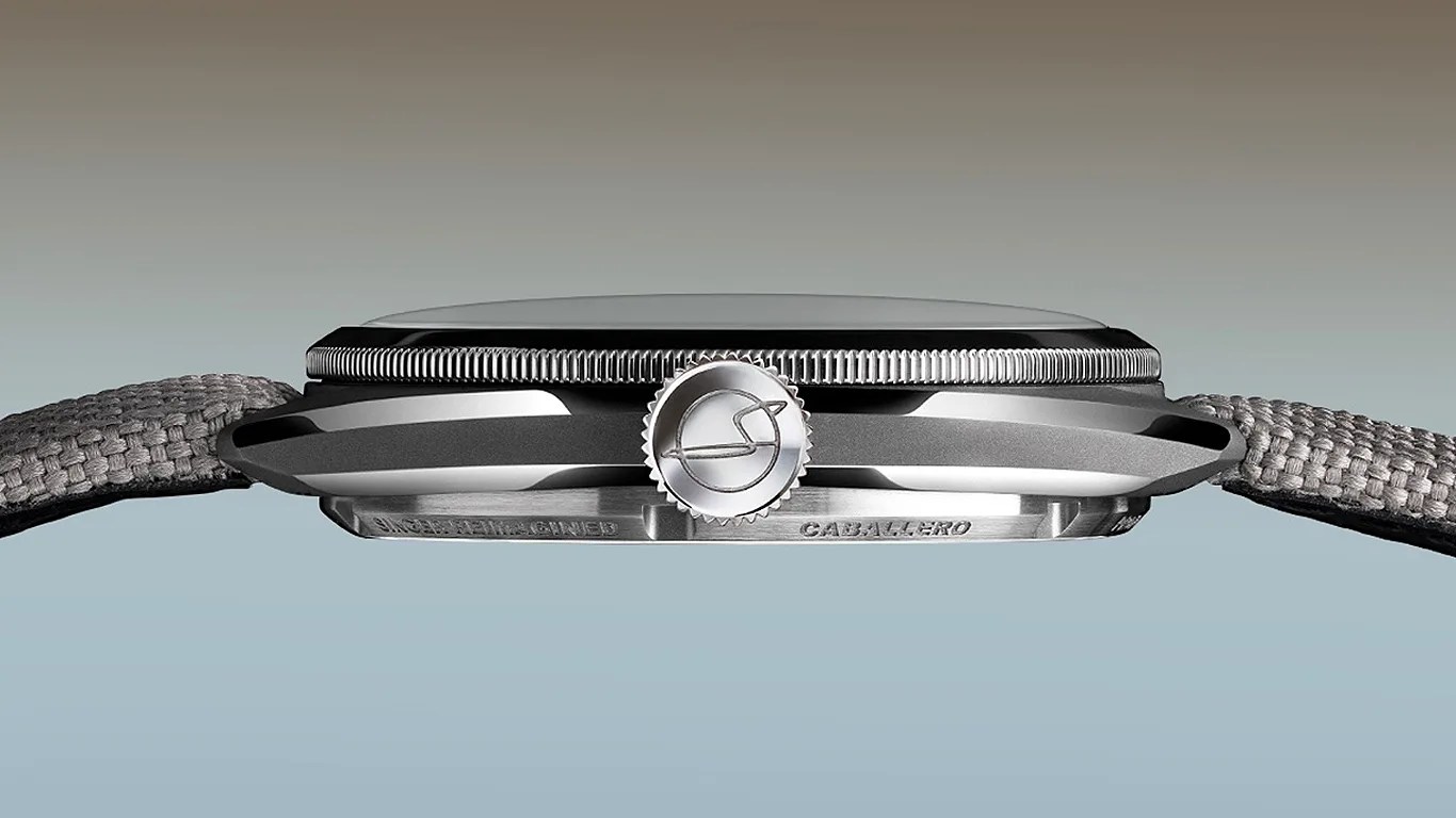 Side view of a silver wristwatch with a textured gray fabric strap and a ridged crown featuring an engraved logo.