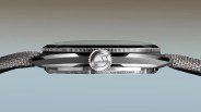 Side view of a silver wristwatch with a textured gray fabric strap and a ridged crown featuring an engraved logo.