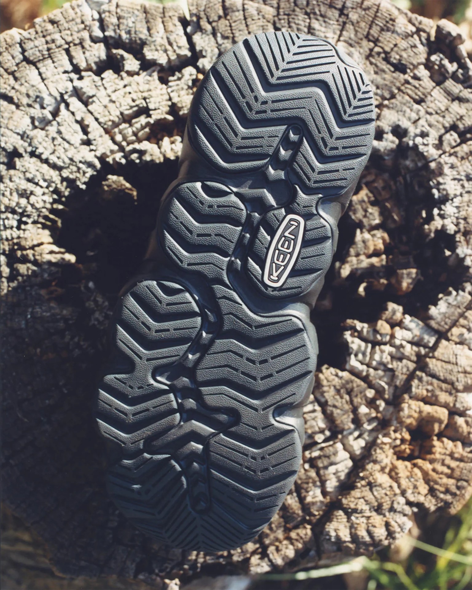 Black rubber sole of a Keen shoe with textured tread pattern on a tree stump.