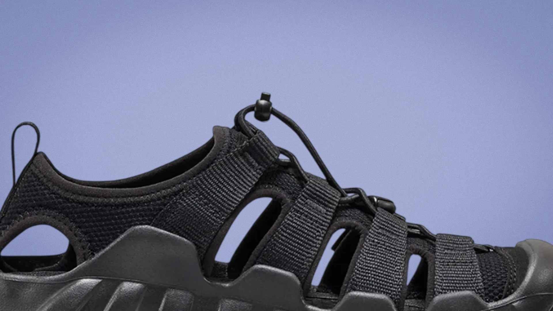 Black outdoor sandal with mesh fabric, adjustable elastic cord lacing, and rugged sole against a blue background.