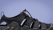 Black outdoor sandal with mesh fabric, adjustable elastic cord lacing, and rugged sole against a blue background.