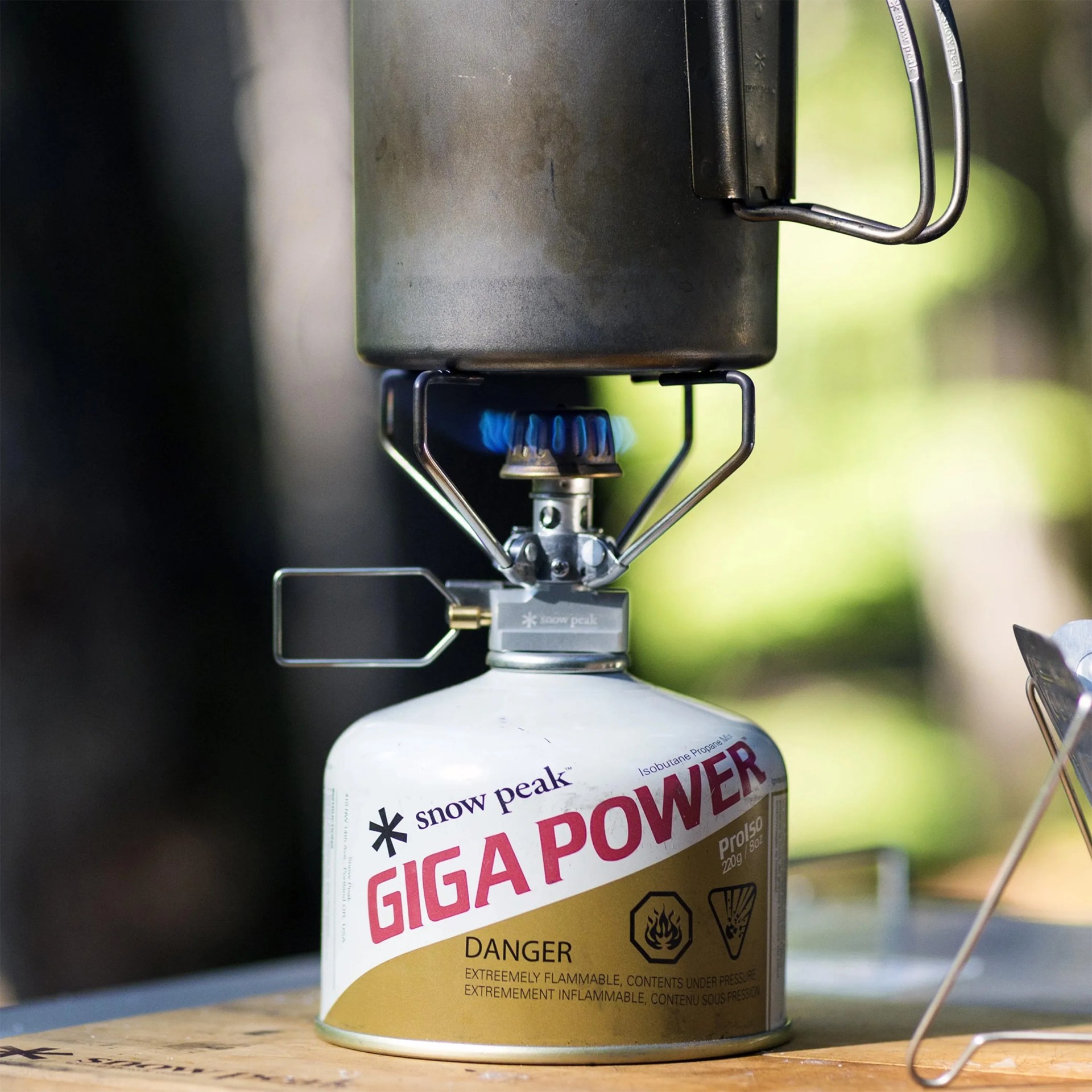White and gold Snow Peak Giga Power portable gas canister with a metal camping stove and pot on top.