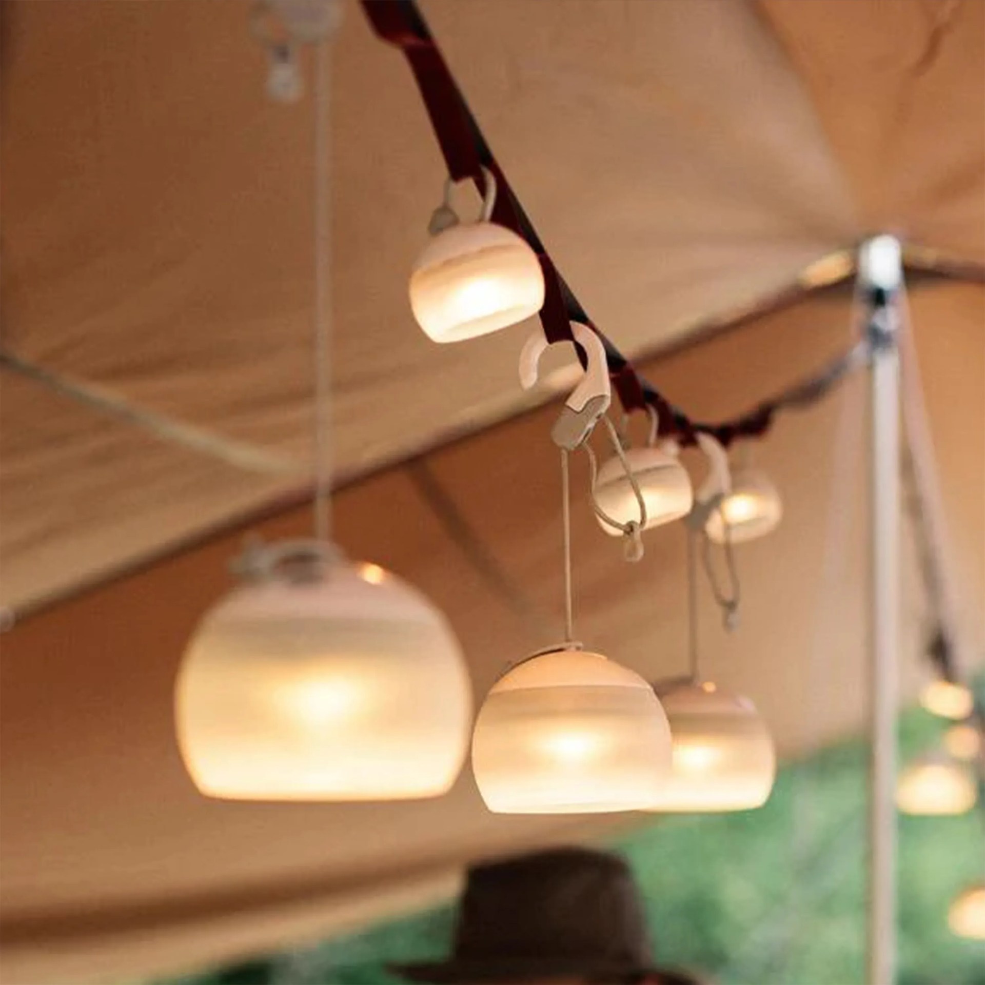 String of small, round, frosted outdoor hanging lights attached to a dark strap under a tan canopy.