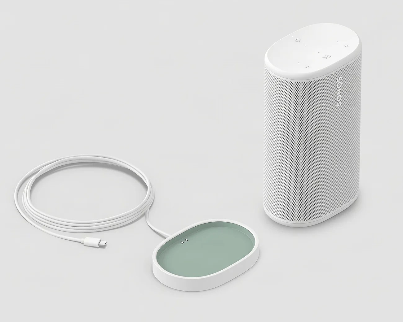 White Sonos speaker with perforated grille and oval wireless charging pad with USB-C cable on a light gray surface.