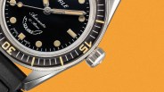 Close-up of a Squale automatic dive watch with black dial, beige markers, and stainless steel case on an orange background.