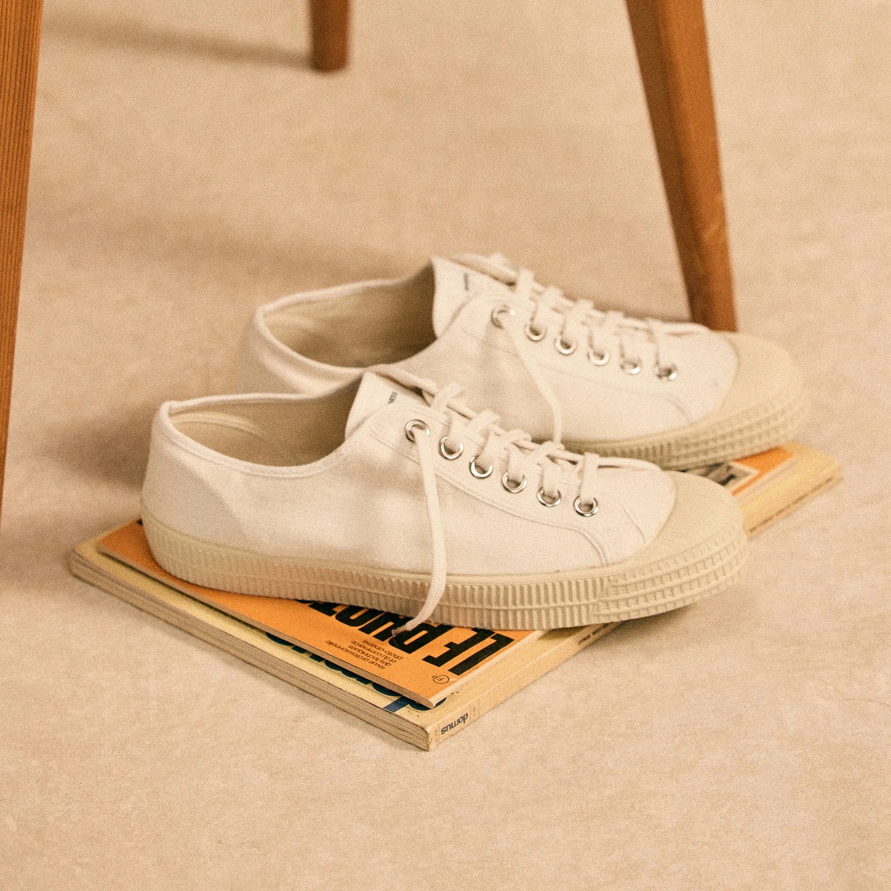 Off-white canvas low-top sneakers with rubber soles placed on stacked books on a beige floor.