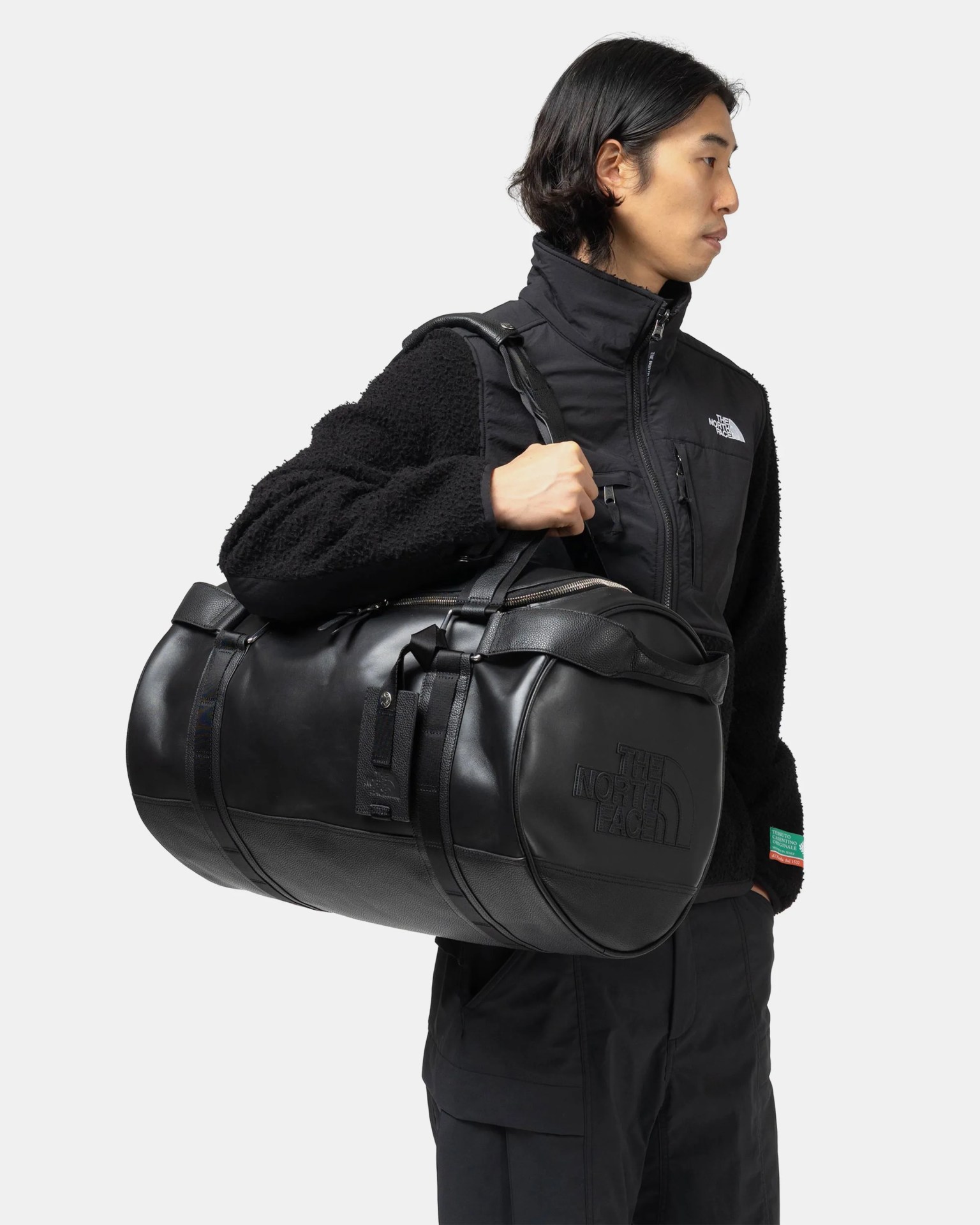 Person holding a large black leather North Face duffel bag over their shoulder.