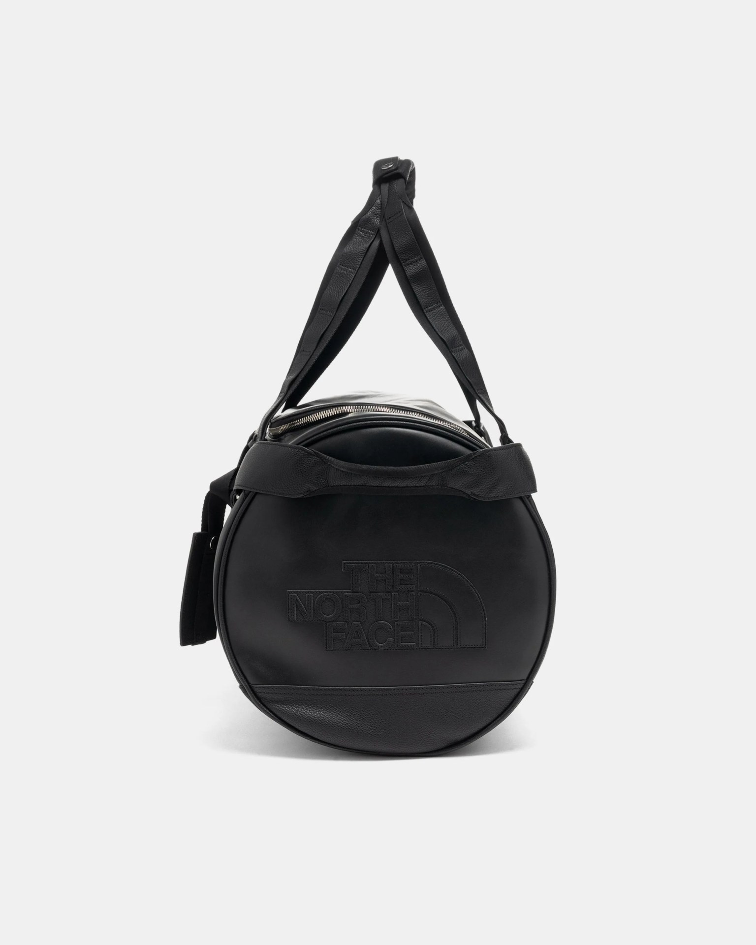 Round black leather duffel bag with embossed "The North Face" logo and dual handles.
