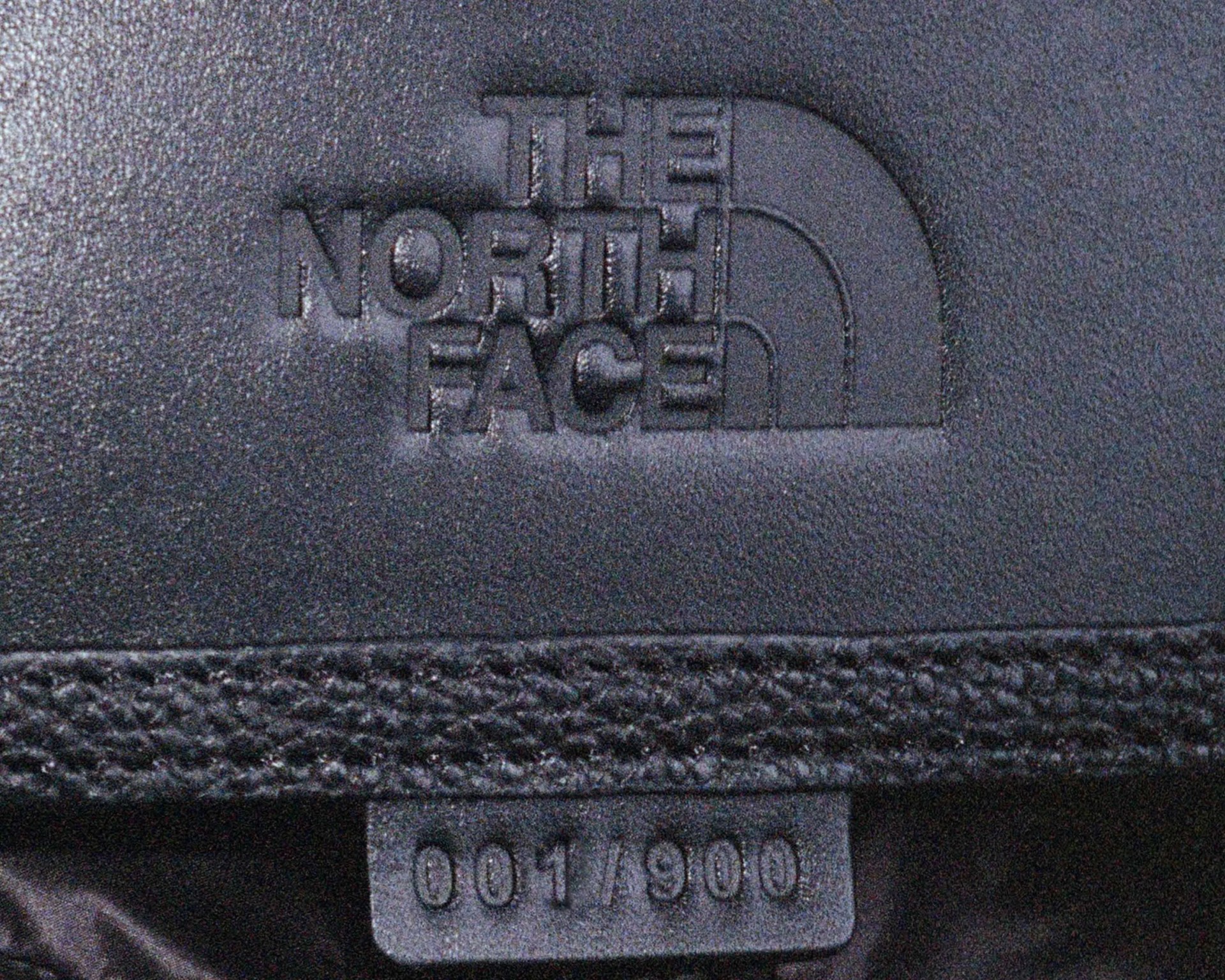 Embossed black The North Face logo on textured fabric with a tag showing "001/900".
