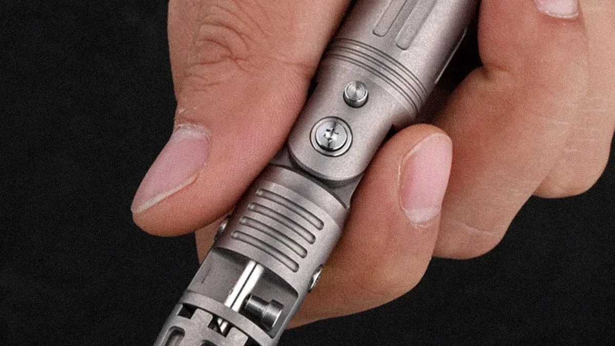 Hand holding a metallic cylindrical device with visible screws and mechanical components.