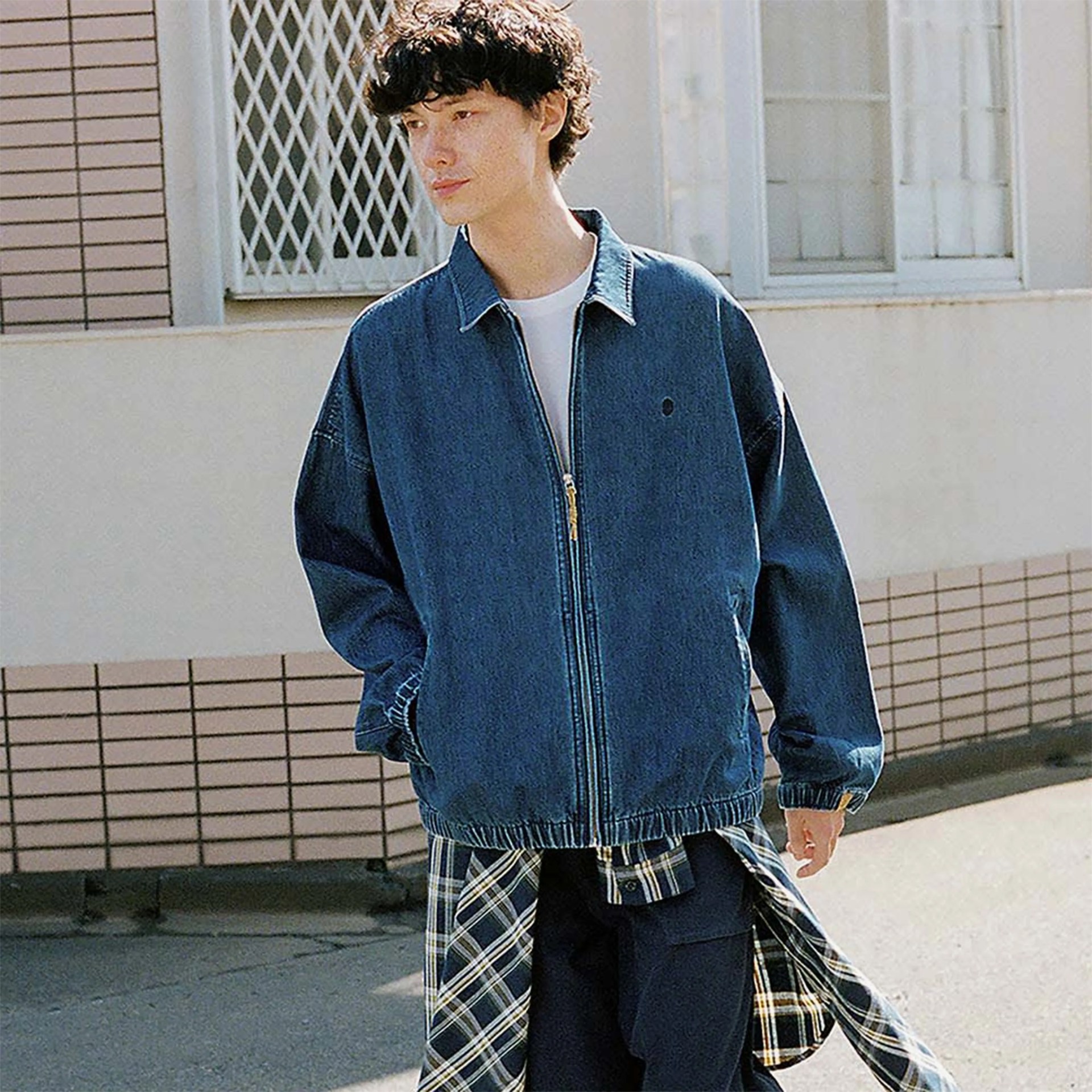 Person wearing a loose-fitting blue denim zip-up jacket over a white shirt and plaid shirt tied around the waist.