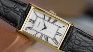Rectangular gold-tone Timex watch with silver dial, black Roman numerals, and black textured leather strap.