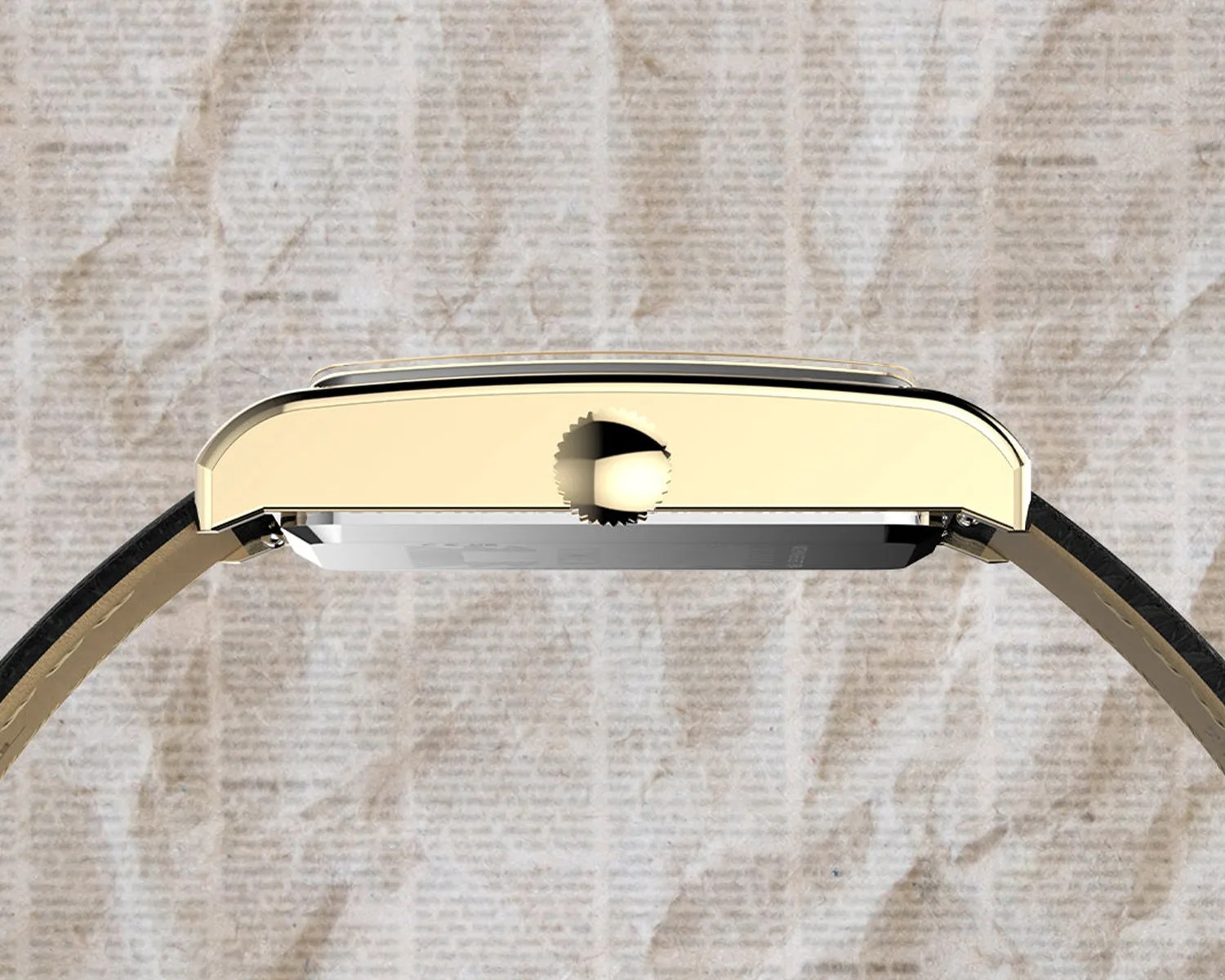 Side view of a rectangular gold watch case with a crown and black leather strap on a textured beige surface.