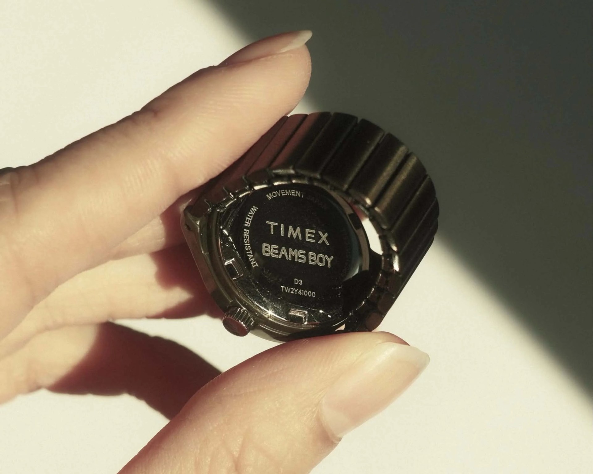 Hand holding a black Timex Beams Boy watch showing the back case with metal stretch band.