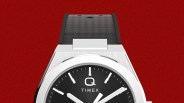 Silver Timex Q watch with black dial and black textured rubber strap on a red background.