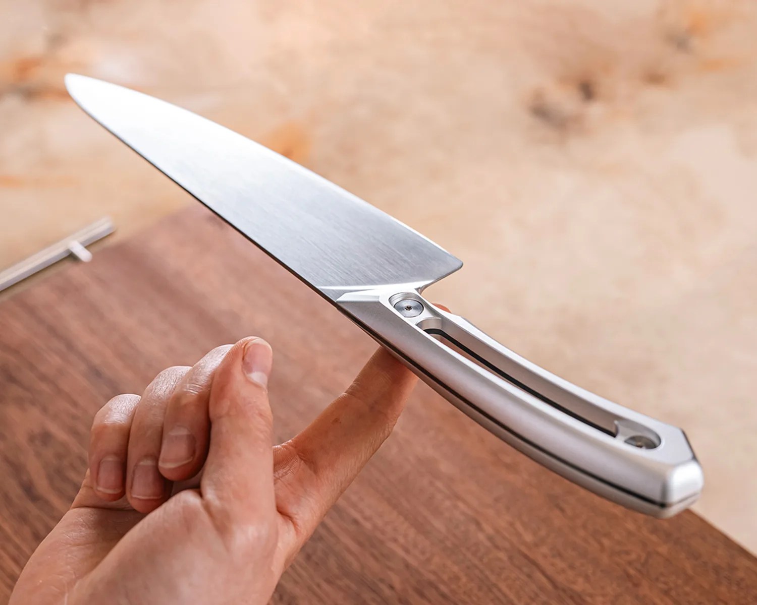 Silver stainless steel knife balanced on a person's finger above a wooden surface.