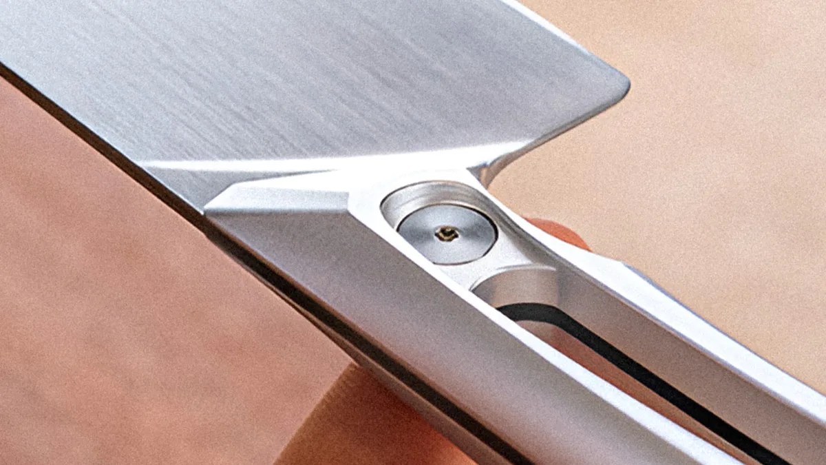 Close-up of a metallic folding knife blade with a visible pivot screw and part of the handle.