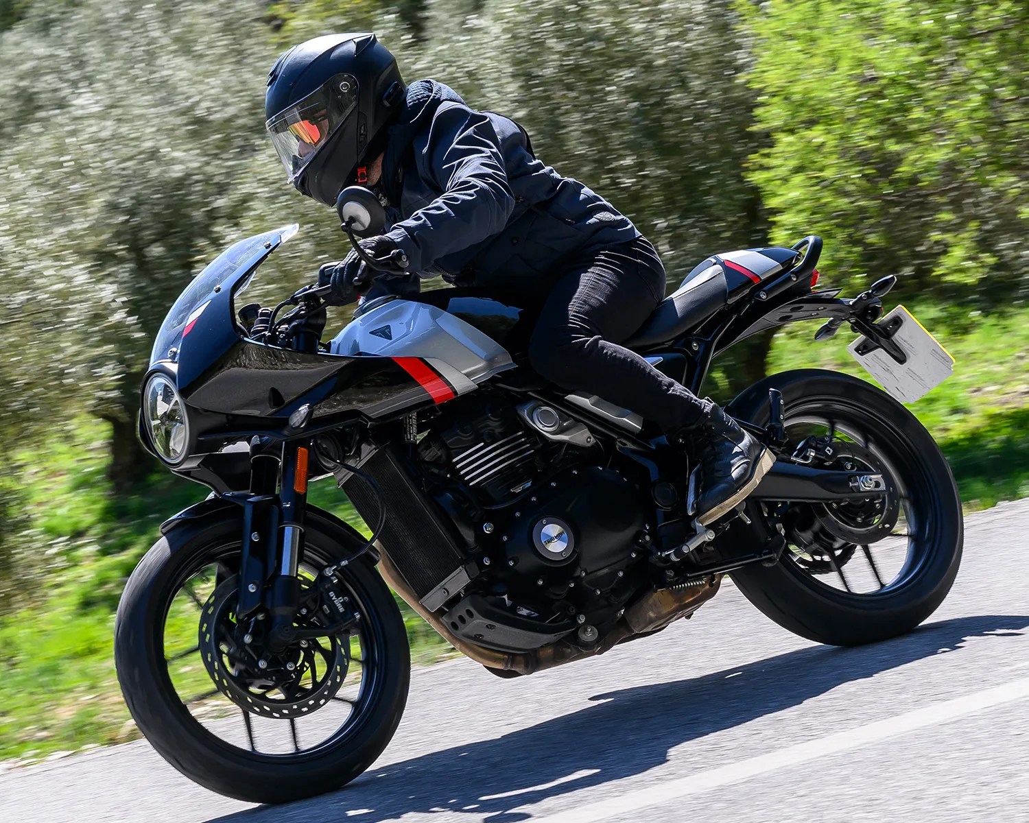 Person wearing black helmet and jacket riding a black and silver sport motorcycle on a road.