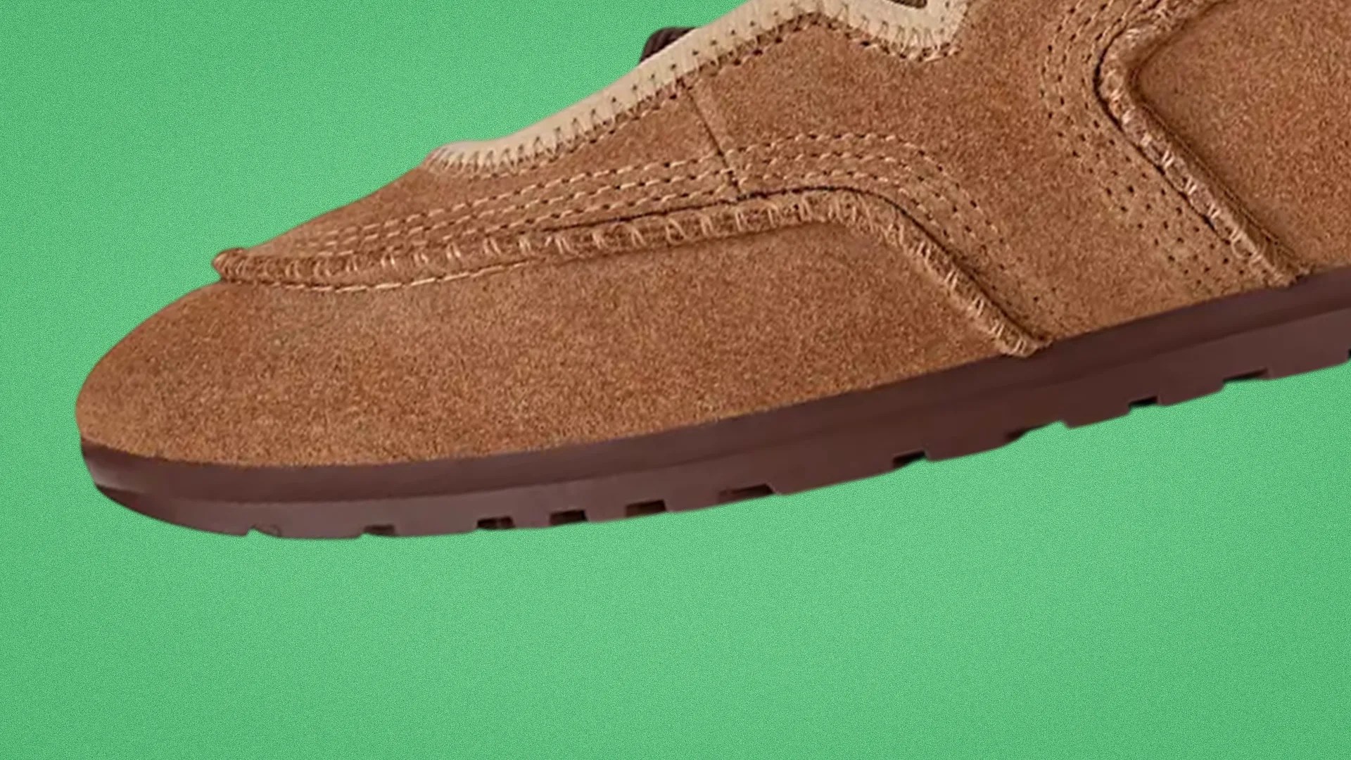 Brown suede moccasin shoe with detailed stitching and a dark brown rubber sole on a green background.